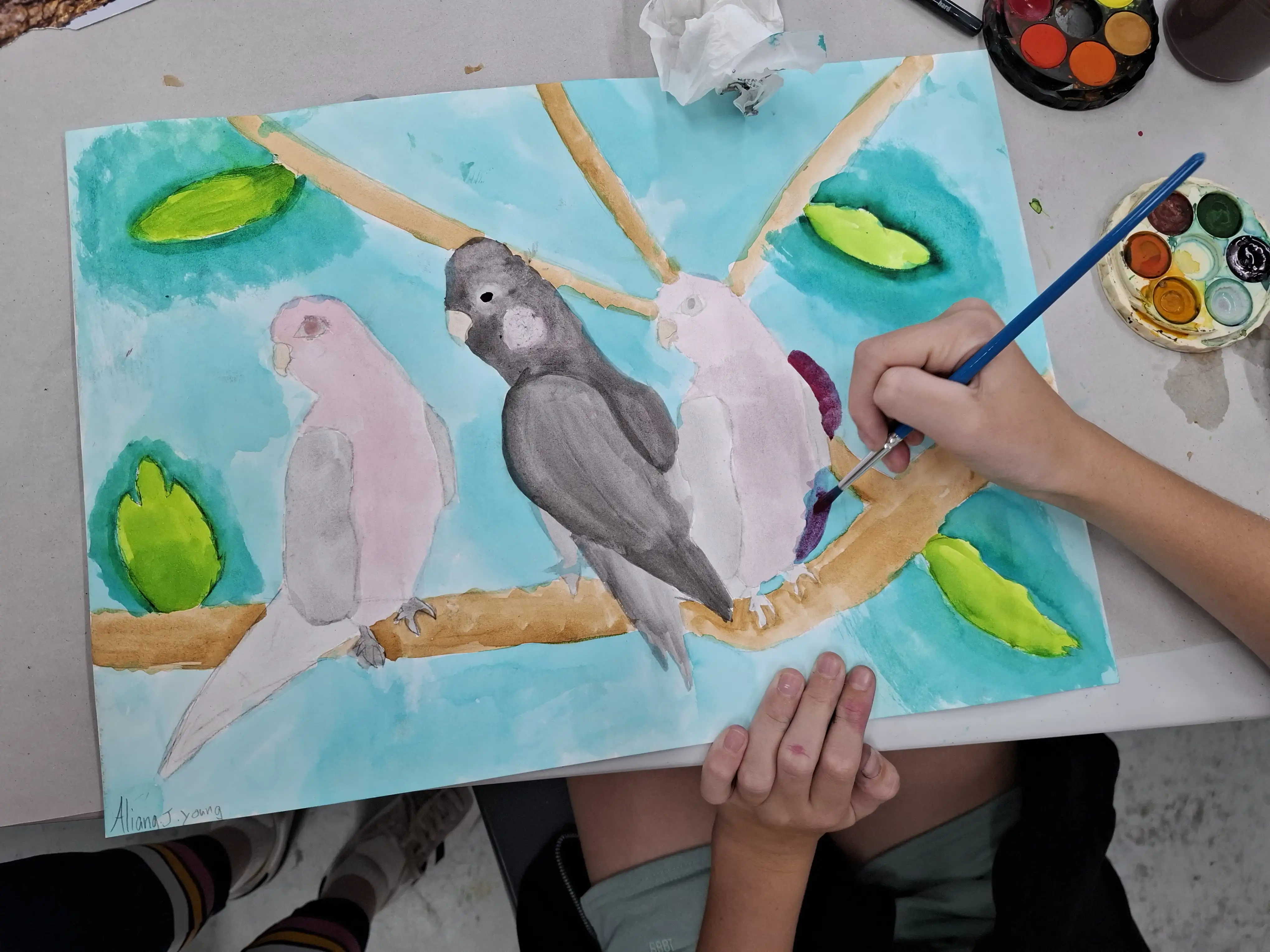 Hands painting birds on a branch using watercolours.